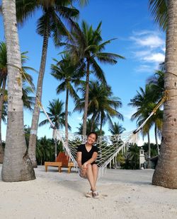 Woman sitting on palm tree at beach against sky