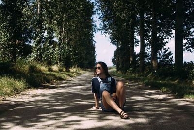 Full length of young woman sitting on footpath amidst trees