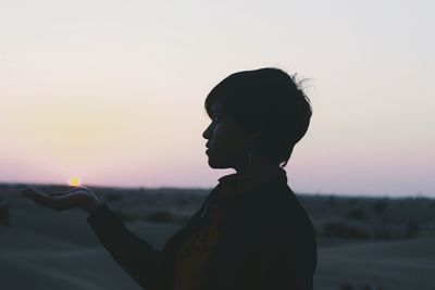 Optical illusion of woman holding sun during sunset against sky