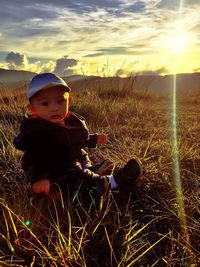 Boy sitting on field against sky during sunset