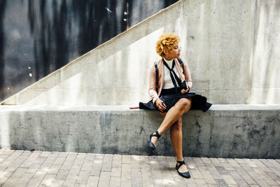 Woman looking away while sitting on retaining wall