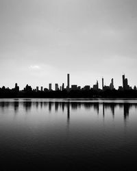 Silhouette buildings by lake against sky in city