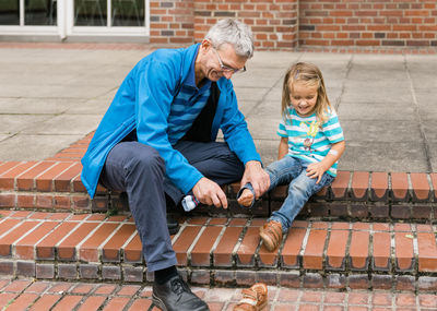 Smiling senior man holding granddaughter leg sitting on steps