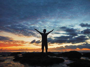 Silhouette man standing on rock by sea against sky during sunset