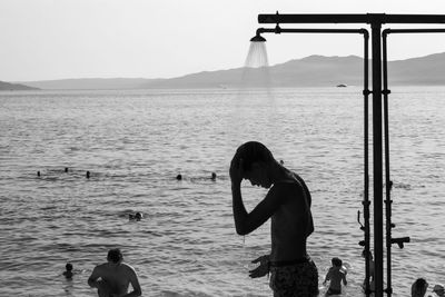 Shirtless man taking shower against lake