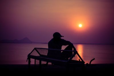 Silhouette man sitting by sea against sky during sunset