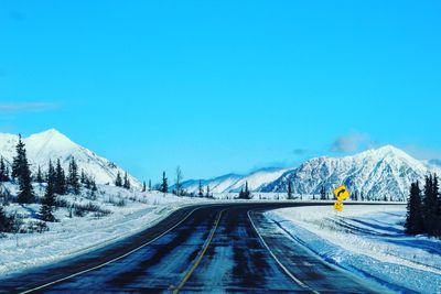 Road amidst snowcapped mountains against clear blue sky