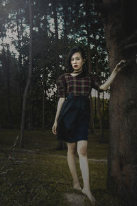 Portrait of woman standing by tree trunk in forest