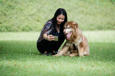 Full length of woman using phone while sitting on grass