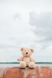 Stuffed toy on rusty metal by lake against cloudy sky