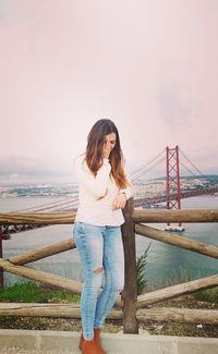 Full length of smiling man standing on bridge over river against sky