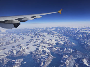 Aerial view of airplane flying over snowcapped mountains against sky