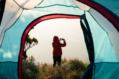 Rear view of man standing on field seen through tent