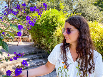 Beautiful young woman wearing sunglasses by flower plants against trees