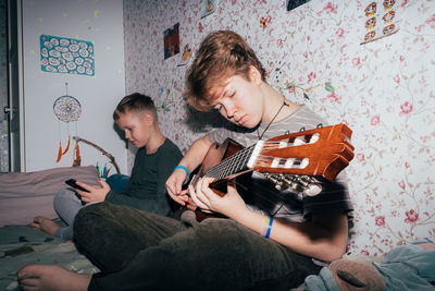 Children spend time, the girl plays the guitar, the boy uses a mobile phone.