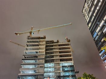 Low angle view of crane by building against sky