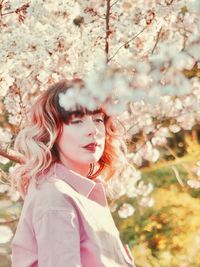 Portrait of young woman standing by cherry blossom