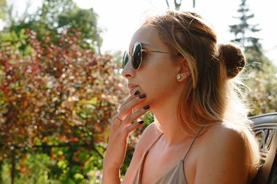 Close-up of thoughtful woman wearing sunglasses while sitting against trees