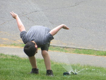 Boy playing with sprinkler on grass in back yard
