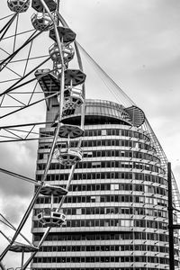 Low angle view of crane by building against sky