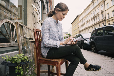 Woman reading paper while sitting on chair against store in city