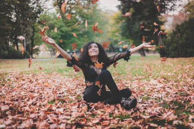 Young woman playing with autumn leaves while sitting in park