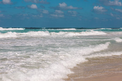 Waves rushing towards shore against sky