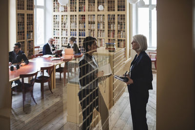 Female lawyers discussing while standing seen through glass in library