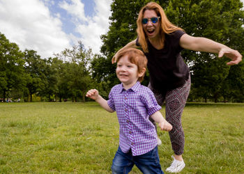 Mother and son running on grass against trees