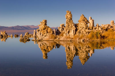 Reflection of rocks in lake against clear blue sky