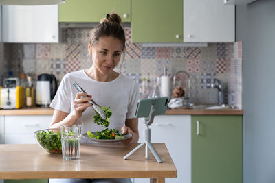 Woman vlogging while preparing salad on table at home