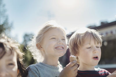 Low angle view of friends eating ice creams at yard on sunny day