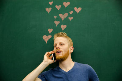 Young man talking on mobile phone with heart shapes on blackboard