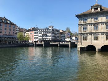 Bridge over river by buildings against clear blue sky