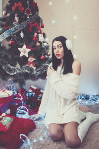 Portrait of young woman sitting on christmas tree at home