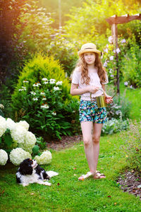 Portrait of smiling girl standing with watering can by plants and dog