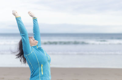 Happy woman raising arms on the beach in winter