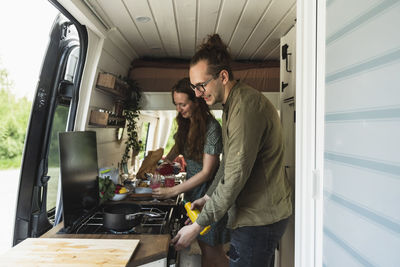 Heterosexual couple preparing food in camping van during vacation