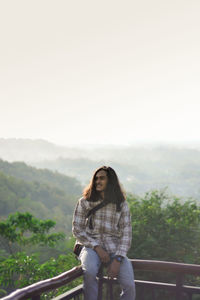 Woman standing on railing against sky