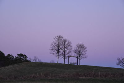 Bare trees on field against clear sky