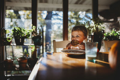 Toddler girl eating breakfast sitting at table in warm sunlight
