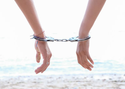 Cropped hands of couple cuffed at beach against clear sky