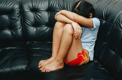 Girl with head on knees sitting on sofa at home