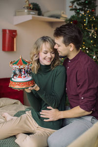 Couple holding small carousel while sitting on bed at home