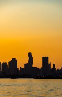 Silhouette buildings by river against sky during sunset