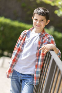 Portrait of smiling boy standing by railing at park