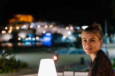 Portrait of woman against illuminated city at night