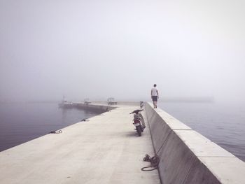 Rear view of man walking on retaining wall at pier in sea during foggy weather