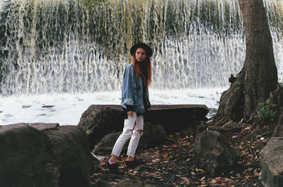 Full length of young woman standing against waterfall in forest