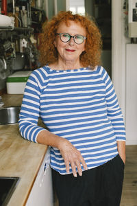 Portrait of smiling senior woman standing with hand in pocket at home